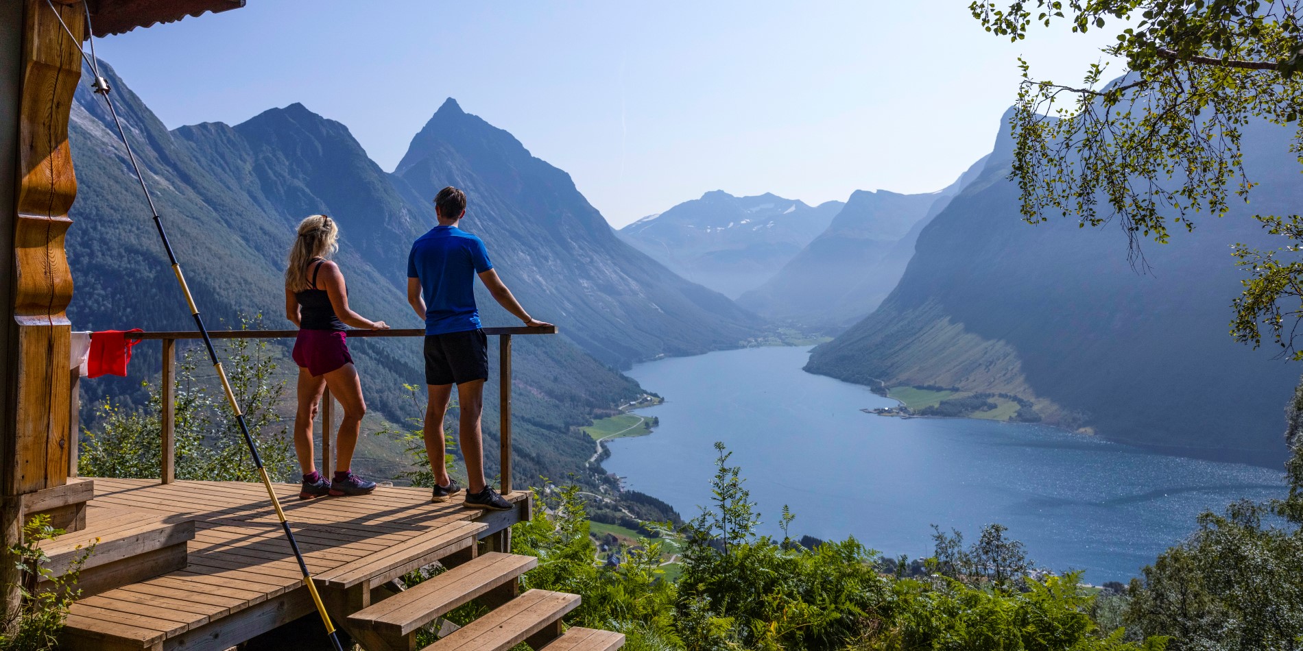 Et par står på et udsigtspunkt og ser ud over Hjørundfjorden. Norges vestkyst