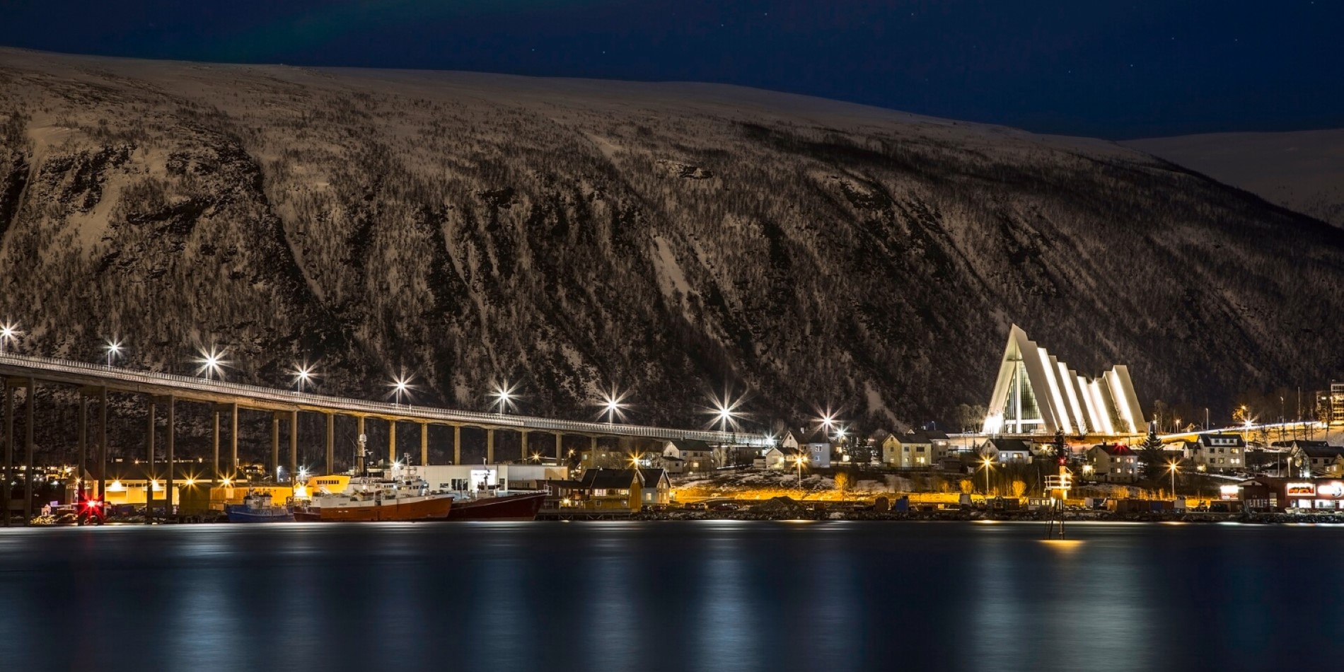 Ishavskatedralen set fra Tromsøya. Det er mørkt, og broen og katedralen lyser op i den mørke nat