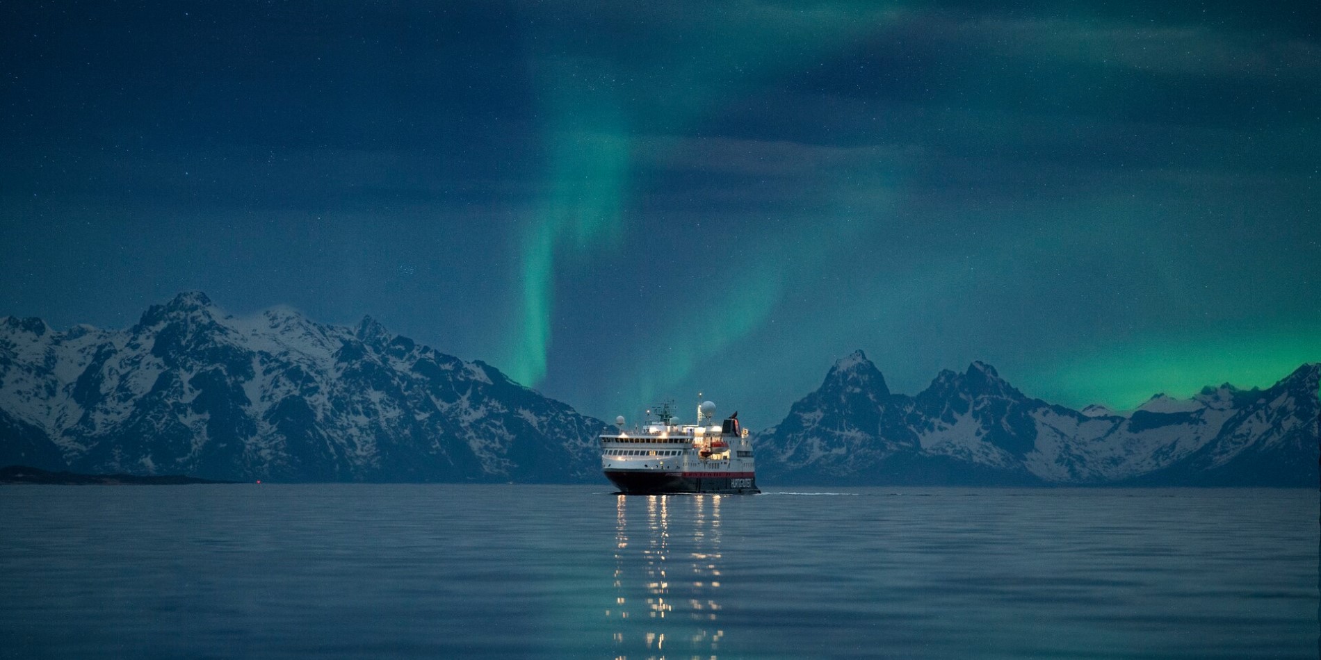 Hurtigrutens skib, der sejler i Norge med nordlyset over sig