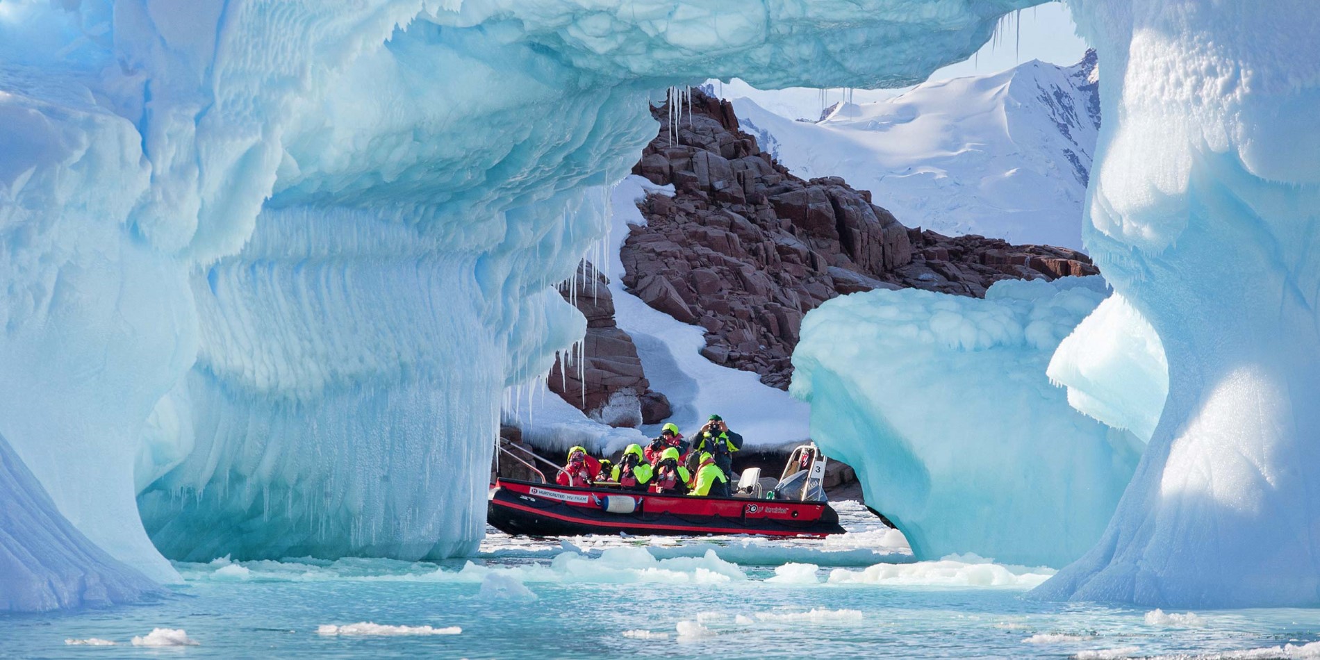Gruppe af turister i lille båd blandt spektakulære isformationer